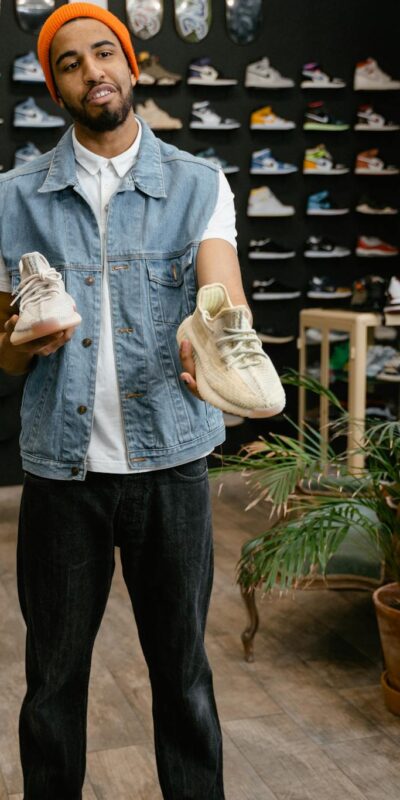 Man showcasing sneakers in a trendy retail fashion store with shoe wall display.