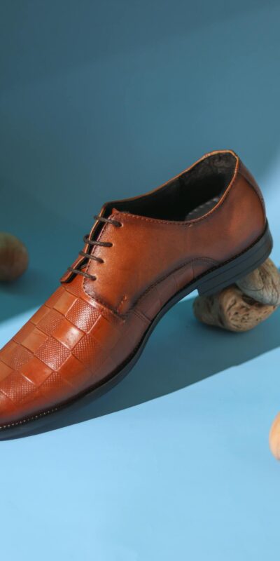 Studio shot of a stylish brown leather men's shoe on a blue backdrop with nuts.