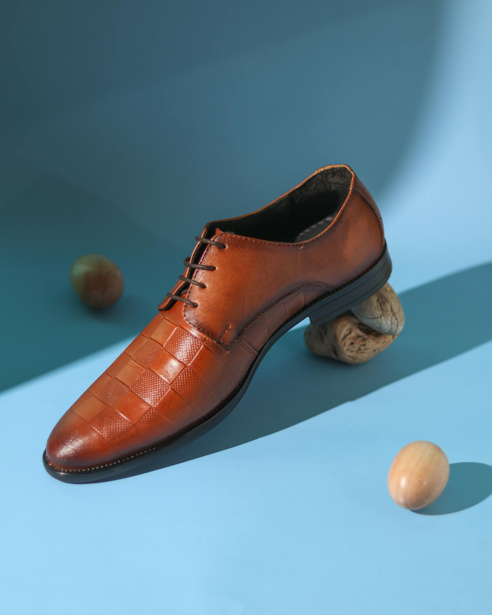 Studio shot of a stylish brown leather men's shoe on a blue backdrop with nuts.